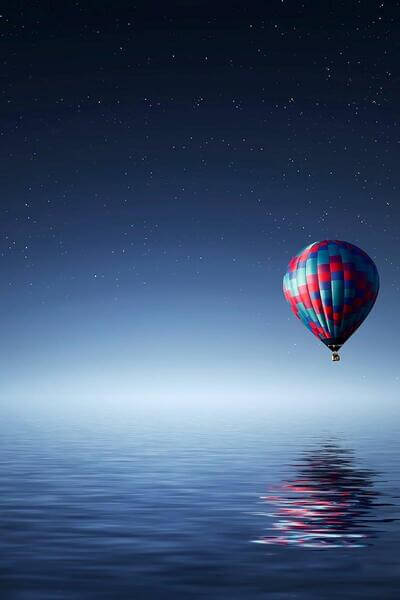 Globo aerostático rojo y azul volando sobre el mar en la noche